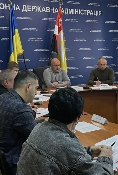 На фото зображено групу людей, які сидять за столом переговорів. На фоні синя вивіска з назвою огранізації та прапори України і м. Рівне