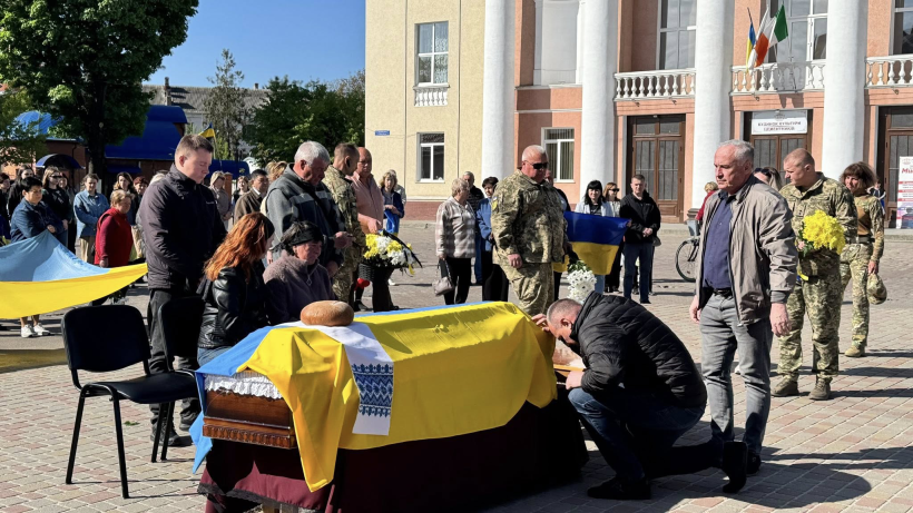 На фото зображено людей, домовину і процес прощання з військовослужбовцем