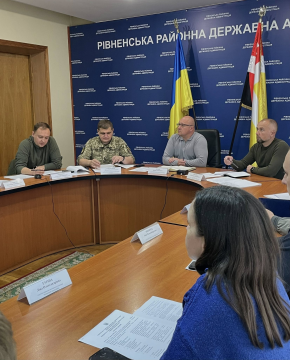 На фото зображено групу людей, які сидять за столом переговорів. На фоні синя вивіска з назвою огранізації та прапори України і м. Рівне