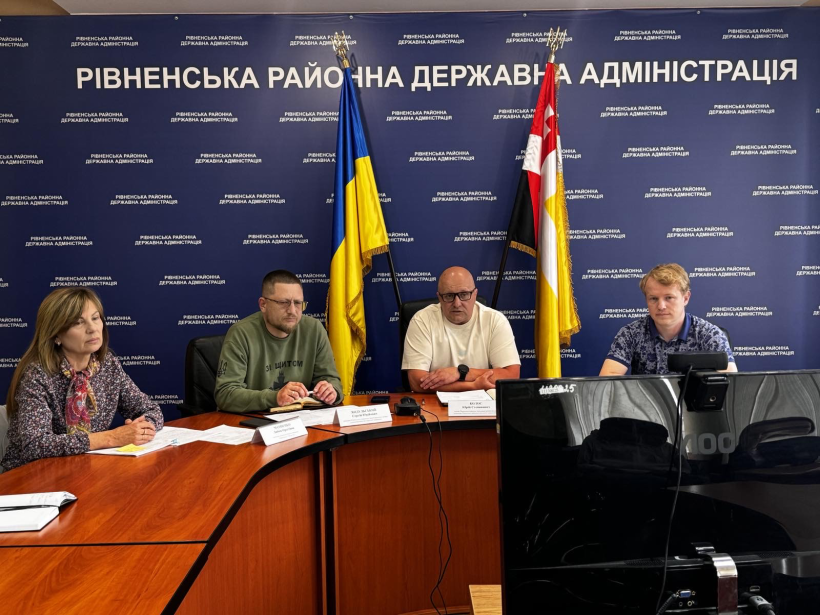 На фото зображено 4-ох людей, які сидять за круглим столом і слухають нараду, на синьому фоні написоно назву установи