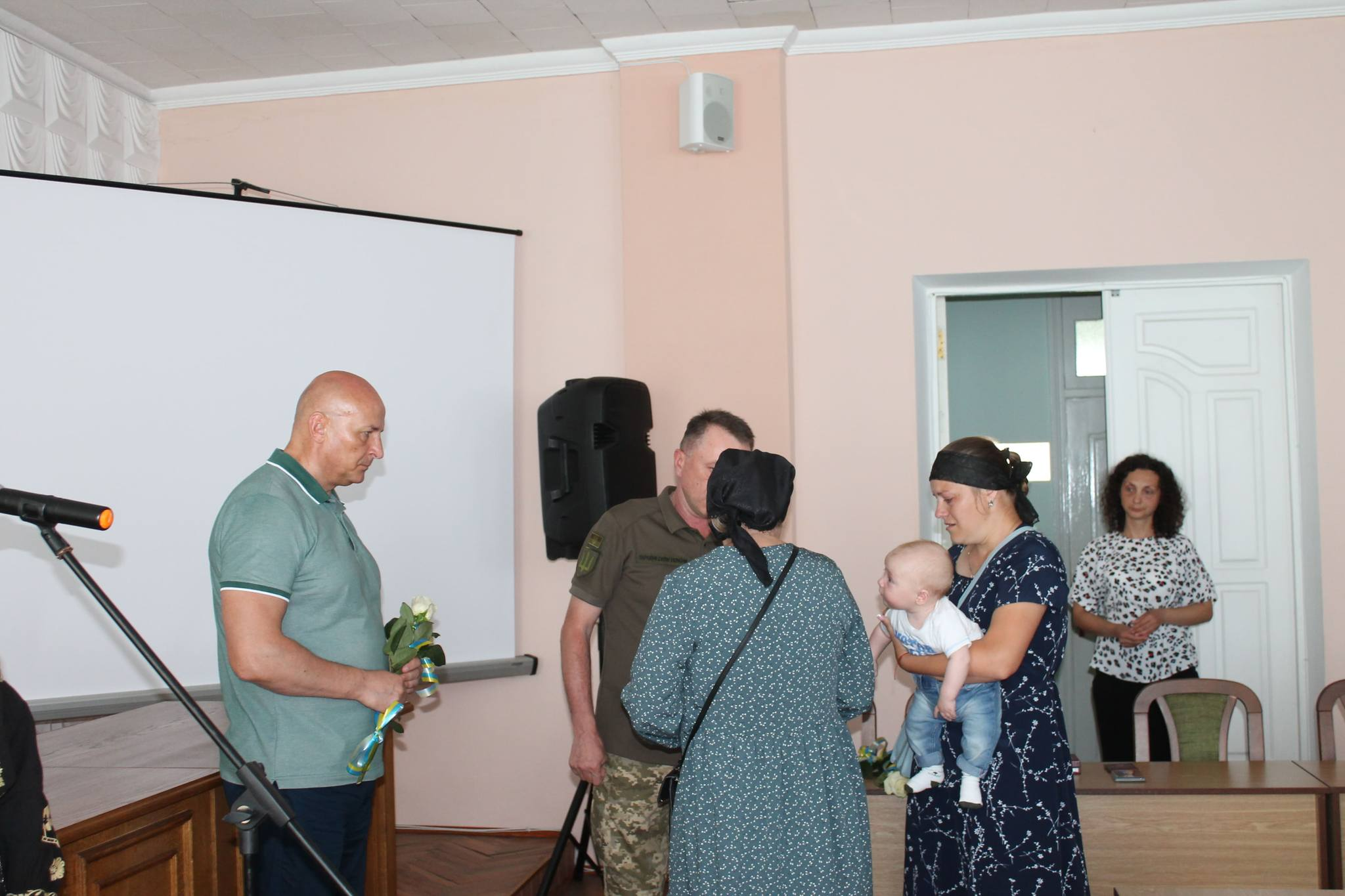 Березнівський міський голова та військовий вручають державну нагороду  рідним полеглого воїна. Матір отримує нагороду, поруч стоїть дружина, яка тримає на руках маленьку дитину.