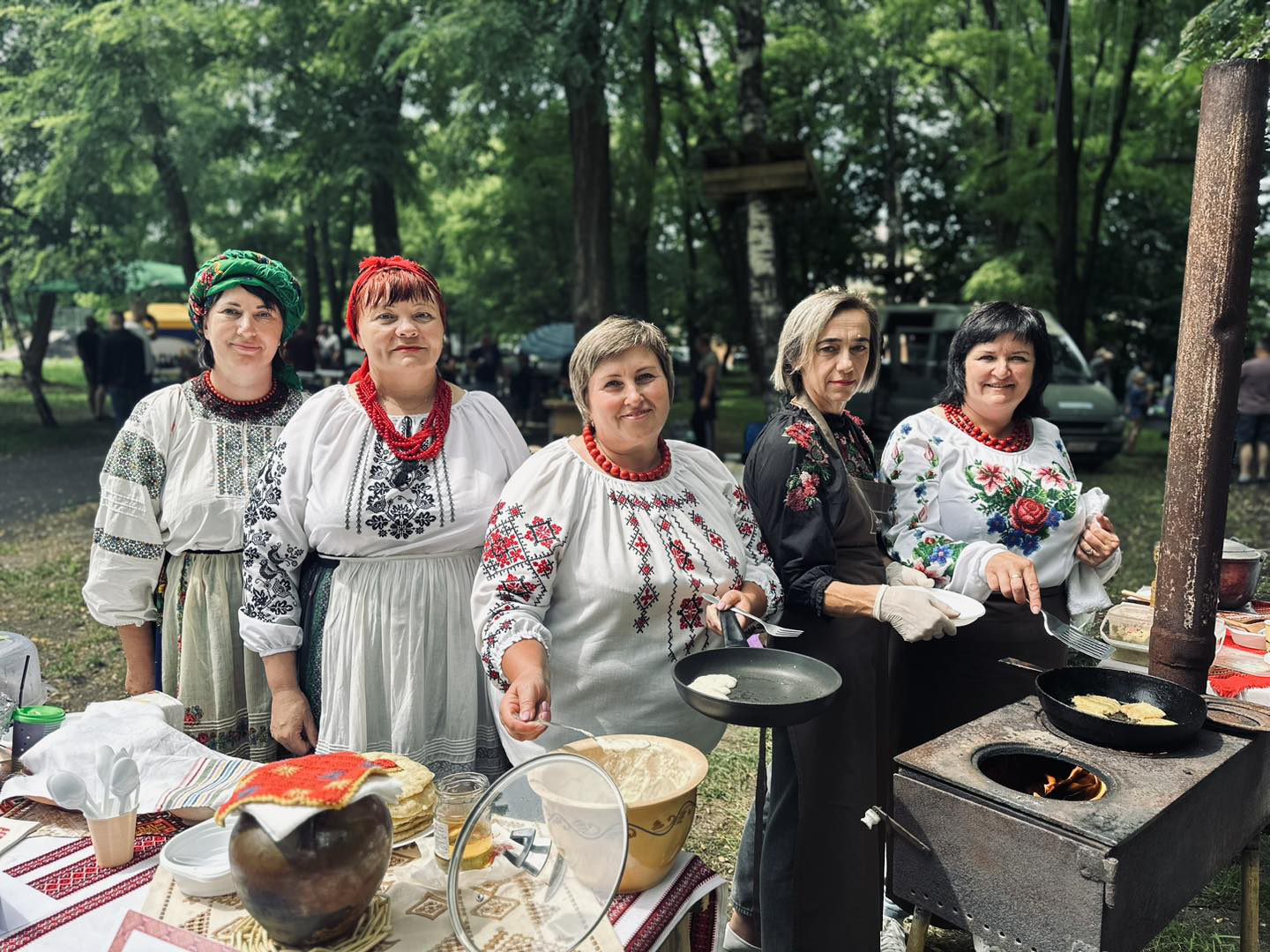 Учасниці ярмарку пропонують гостям смаколики. П'ять усміхнених жінок в українських національних костюмах та намисті.