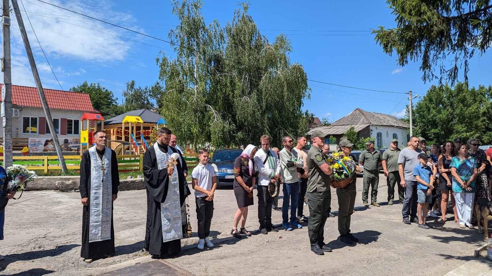 Перед Алеєю загиблих Героїв стоять військові з корзиною квітів, священнослужитель та мешканці села Городище