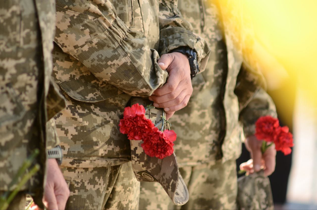 Стоять військові і тримають у руках гвоздики