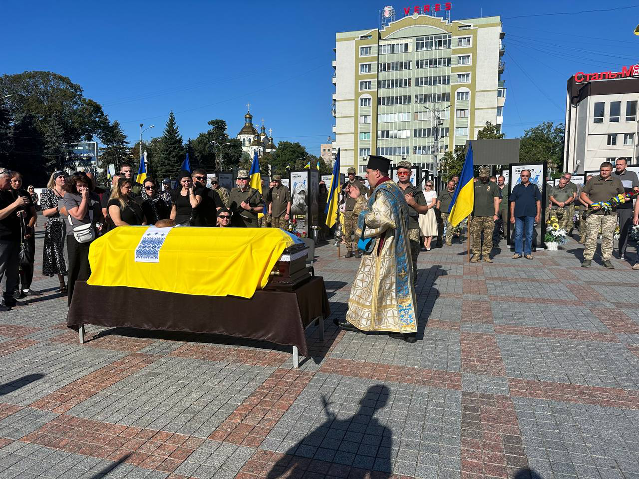 Майдан Незалежності м.Рівне. Стоїть труна з полеглим воїном накрита жовто-блакитним прапором біля якого стоять рідні загиблого Захисника, священник, військовослужбовці та рівняни.