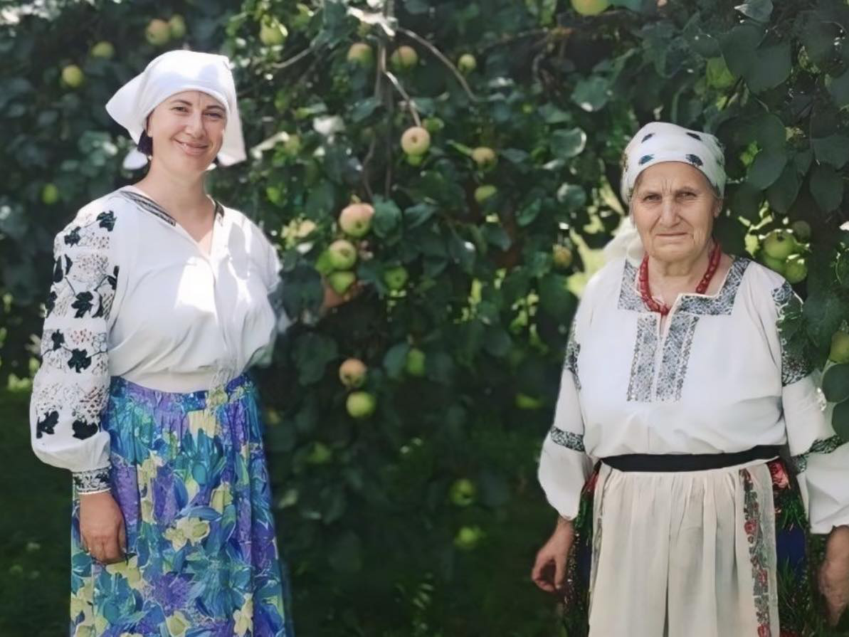 Дві жінки в національних костюмах стоять біля яблуні