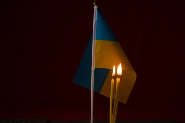 На фото зображено український прапор на чорному фоні, а поруч горить 3 свічки